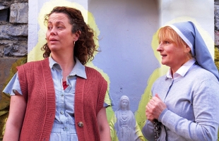 Poster for Philo, Neilí Conroy in a red cardigan and Niamh McGrath, dressed as a nun, are both facing right with a bright yellow glow around them, and a statue of the virgin Mary in the background.