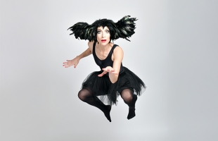 Sarah-Louise Young dressed in a black feathered head-dress, and black leotard leaping mid-air
