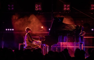Bill Laurance sat on stage at a grand piano with moody red/purple lights, and slight haze
