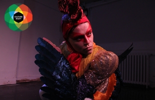 Production still of 'Chicken' - Eva O'Connor dressed as a cockerel looking over her right shoulder at the audience