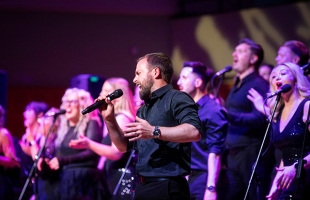 A group of singers, dressed in black, with microphones, singing passionately