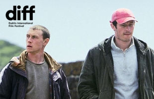 Nick (1917’s George MacKay) and Liam (Callum Turner), stand outside in a open landscape, they both have worried, confused looks on their faces.