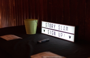 A light box with the words STORY SLAM on the top line, and on the bottom line SIGN UP! with heart emojis either side.