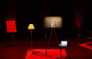 The image shows Pavilion Theatre's stage, with a lamp, microphone and an easel with an image that reads