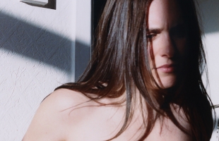 Close-up of Ellie O'Neill who has long brown hair, partially lit by strong sunlight and shadows, looking thoughtfully toward the camera