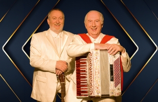 Foster & Allen in coordinated cream suits pose with guitar and accordion in a studio portrait.
