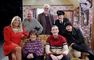 The main cast of Give My Head Peace all smiling at the camera sat on the set of the TV show.