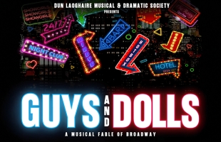 Title image for Dún Laoghaire Musical & Dramatic Society's production of Guys & Dolls. We see a large neon text in the foreground with the title, against a black background with lots of bright coloured graphics of neon city signs for motels, bars & clubs.