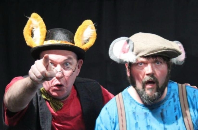 A performer dressed as a fox wearing a bowler hat, and bow tie points, with another performer dressed as a mouse looking where he is pointing