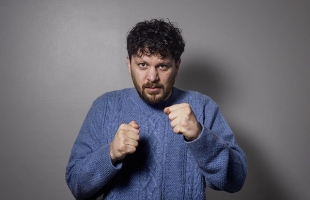 Killian Sunderman, wearing a blue knitted jumper, holds his hands up, in fists, like a boxer