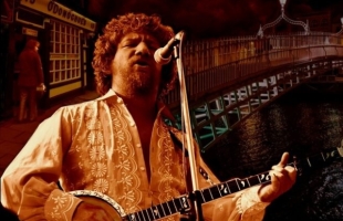 Chris Kavanagh as Luke Kelly, playing the guitar, with a traditional Irish pub, and the Ha'penny bridge behind him