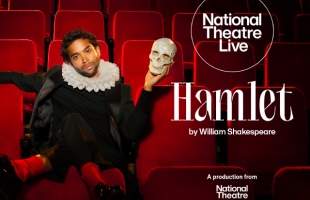 Hiran Abeysekera dressed in a black outfit, with a victorian ruff, sits in theatre seats, holding a skull