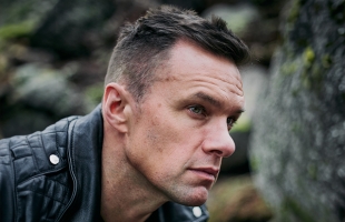 Niall Breslin with a short back and sides, wearing a black leather jacket, staring pensively off to the side.