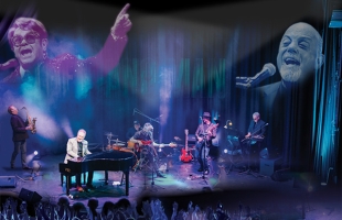 John Forde sits on stage at the piano alongside The 52nd Street Band, there is a bluey purple lighting and an image of Elton John & Billy Joel is projected behind them.