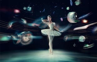 A female ballet dancer, en pointe, dressed in a white corset and tutu, with a tiara, stands surrounded by whirring clock-faces, all pointing to midnight
