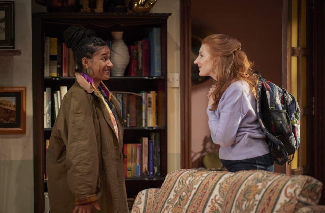 Fanta Barrie, dressed in a large green overcoat, and Mags McAuliffe, dressed in a purple jumper with backpack, smile at each other