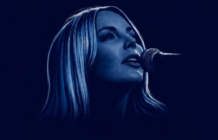 The singer sings into a microphone, illuminated in deep blue light.