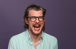 Tony Cantwell wearing thick-rimmed glasses and a pale green shirt, appearing to yell with joy.