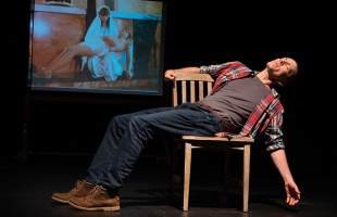 Jay Sefton lays back sideways on a wooden chair, with his left arm outstretched. An image of the Pieta is projected behind him, and you can see that Jay is holding the same pose as Jesus