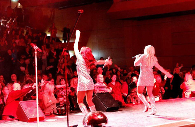 A picture of two female singles dressed in 60s style, performing in front of a large crowd