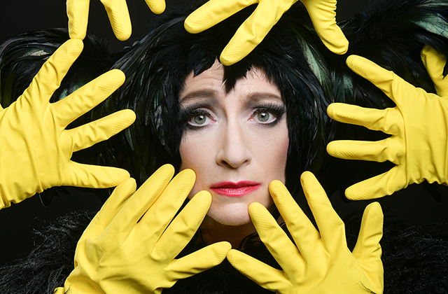 Sarah Louise You in An Evening Without Kate Bush, she is picture upclose with lots of hands wearing yellow rubber gloves encircled around her face