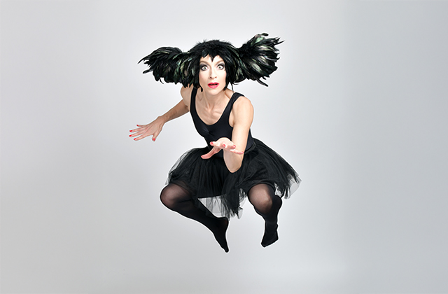 Sarah-Louise Young dressed in a black feathered head-dress, and black leotard leaping mid-air