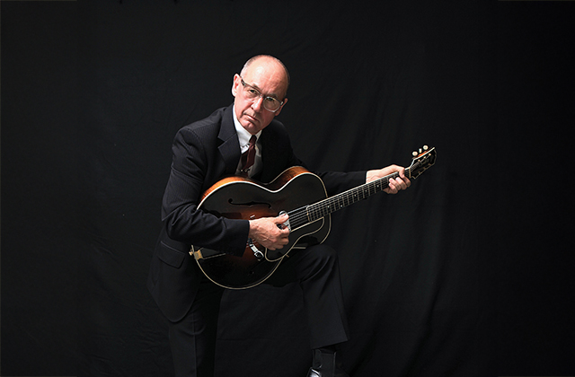 Andy Fairweather Low dressed all in black, holding a guitar