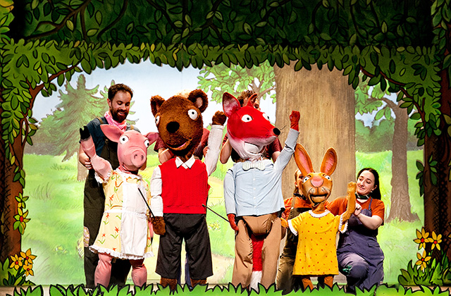 All the friends from Acorn Wood are standing together on stage, they is a pig, squirrel, fox and rabbit. They are waving towards the camera