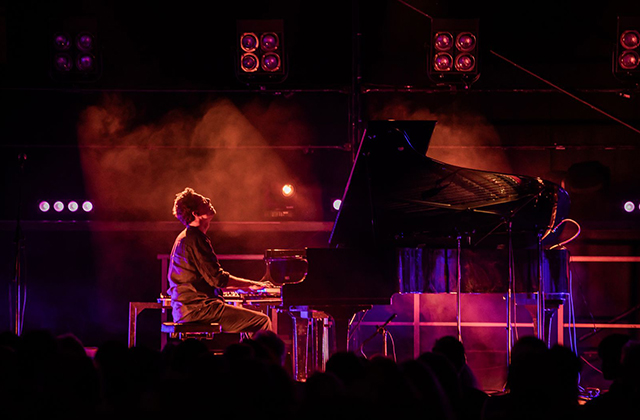 Bill Laurance sat on stage at a grand piano with moody red/purple lights, and slight haze