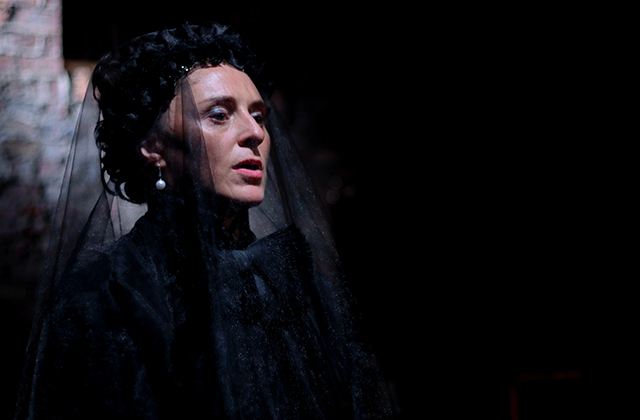 Mary Murray as Cosima, dressed all in black with a black veil over her face