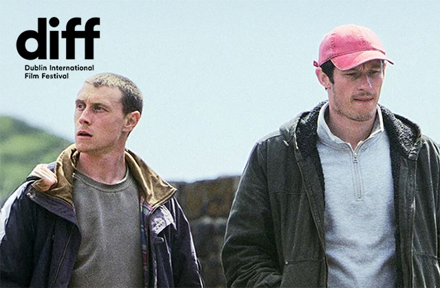 Nick (1917’s George MacKay) and Liam (Callum Turner), stand outside in a open landscape, they both have worried, confused looks on their faces.