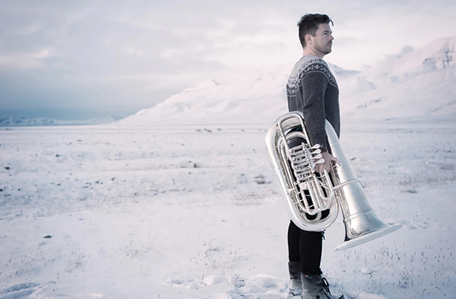 Daniel Herskedal stands on a snow covered landscape, holding a tuba