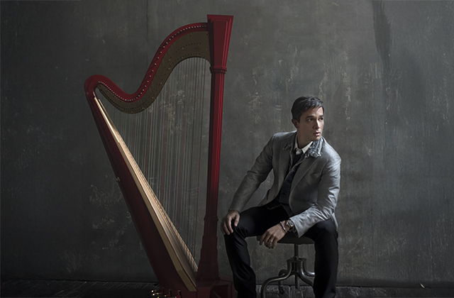 Emmanuel Ceysson sits in a grey suit, with a large red harp