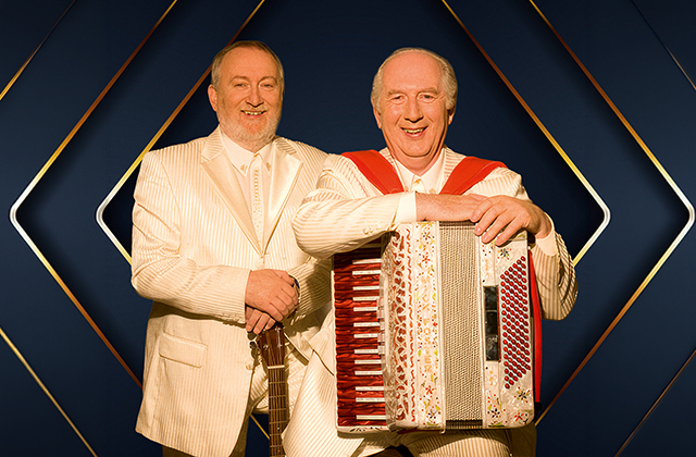 Foster & Allen in coordinated cream suits pose with guitar and accordion in a studio portrait.
