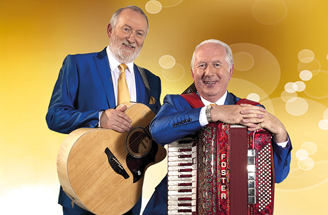 Allen, standing holding his guitar, and Foster sitting with his accordion on his lap, both wearing blue suits and smiling