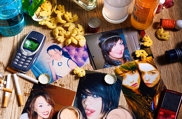 A flat-lay arrangement of early 2000s teenage youth culture items on a wooden table. It features scattered printed photos of young women with Y2K and emo hairstyles, a classic blue Nokia 3310 mobile phone displaying a text notification, and a red Sony MP3 player. Surrounding the photos are scattered corn snacks, cigarettes, matches, loose tobacco, bottle caps, an orange Bacardi Breezer bottle, nail polish, and makeup compacts.