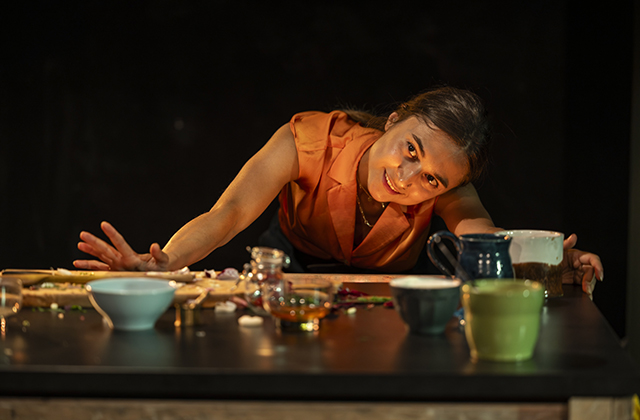 Isabella Nefar, a young Persian woman, leans over a table filled with pots and jugs. She is smiling.