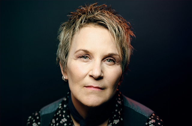 Mary Gauthier is pictured up close, against a black background. Her short hair is styled, with blonde highlights.
