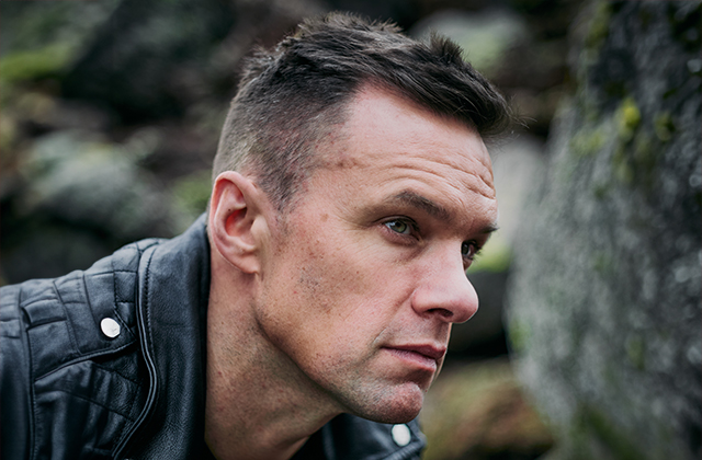 Niall Breslin with a short back and sides, wearing a black leather jacket, staring pensively off to the side.