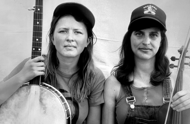 Nora Brown holding her banjo, and Stephanie Coleman with her fiddle, smiling in black and white
