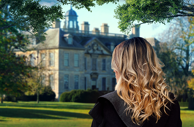 A woman with long wavy blonde hair stands in a sunlit garden, looking toward a large historic mansion framed by trees.
