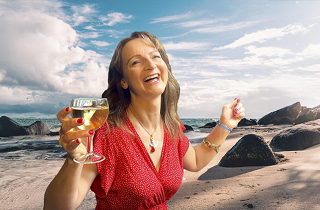 Norma Sheahan as Shirley Valentine. Smiling with a glass of white wine, with a sunny beach behind her