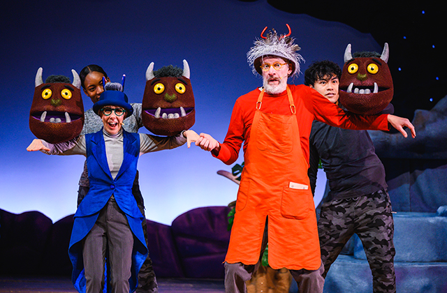 2 performers, one in blue and one in red, hold hands while puppeteers use Gruffalo heads around them
