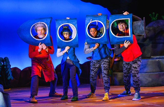 4 performers hold painted cardboard panels in front of their faces, which makes it seem they are looking out the windows of a spaceship