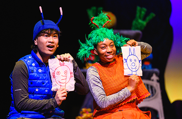2 performers, one in blue and one in red each hold up a cartoon drawing of the others' character