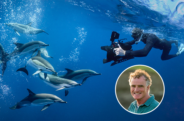 Ken O'Sullivan swims alongside a pod of dolphins in clear blue ocean water while filming with a professional camera rig. A circular inset in the corner shows him smiling outdoors.