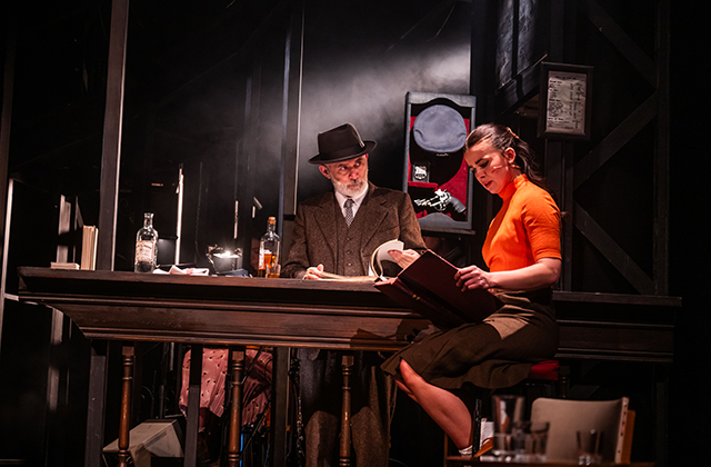 Tommy Tiernan & Tabitha Smyth from The House Must Win, Together they sit at a table, Tabitha is reading and Tommy is staring at her intensely