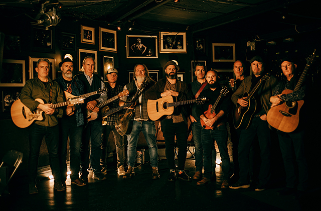The full band of White Horse Guitar Club, stood in a dimly lit room holding their instruments