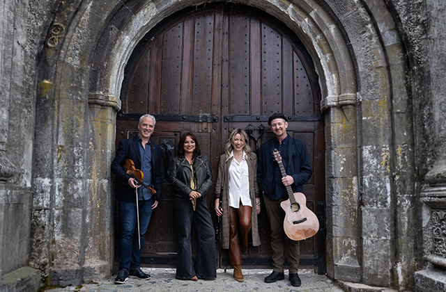 From left to right Tom Morrow, Pauline Scanlon, Muireann Nic Amhlaoibh and John Doyle stand together in a line, smiling towards the camera, in front of a large castle door